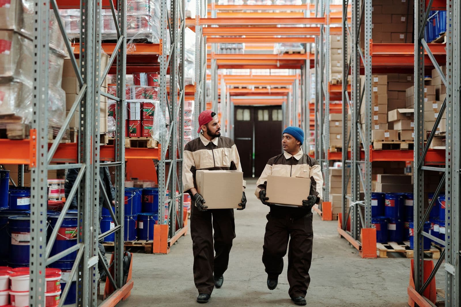 Two workers carrying parcels along a warehouse aisle