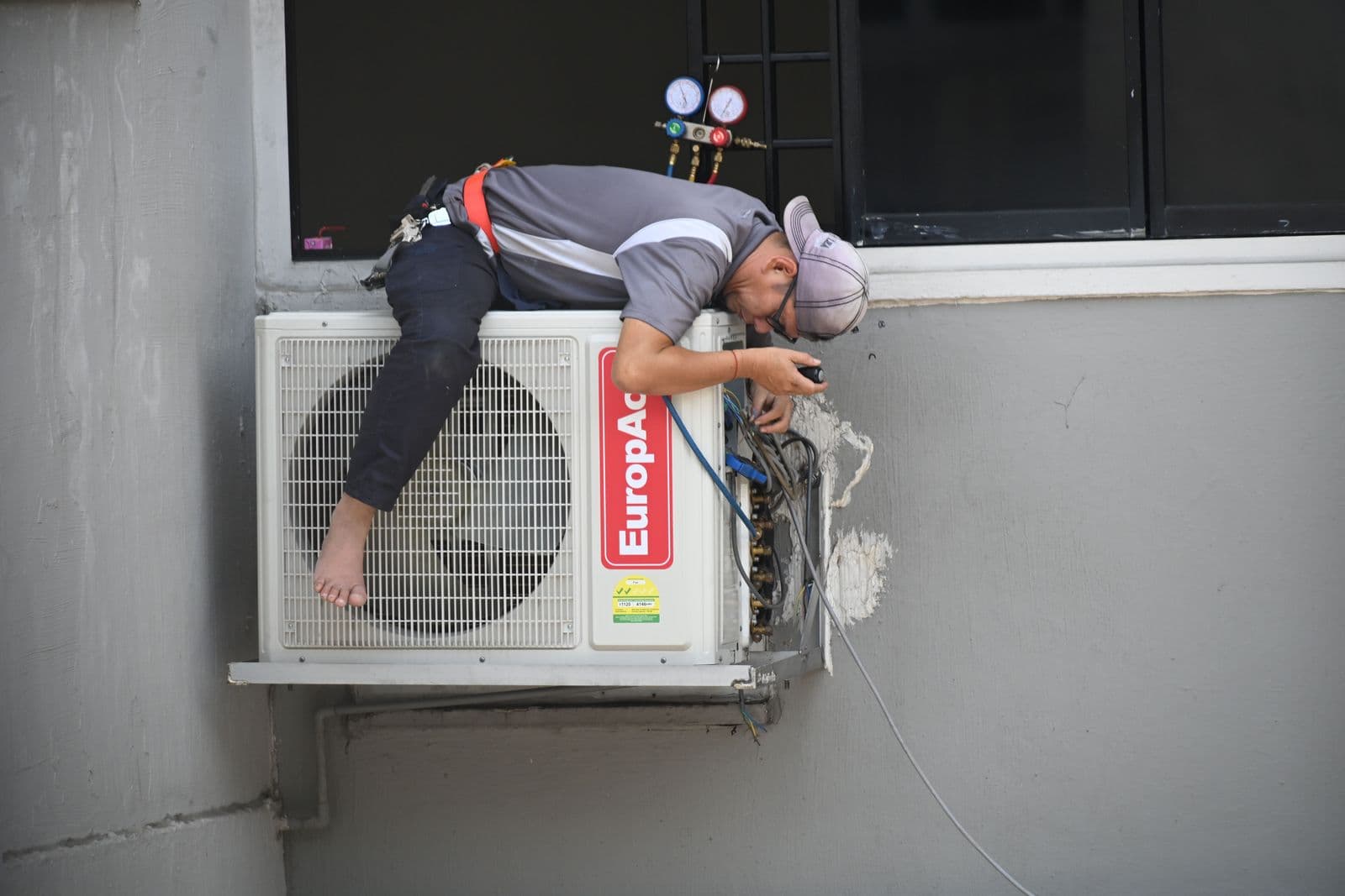 A technician servicing an outdoor air-conditioning unit mounted on a wall