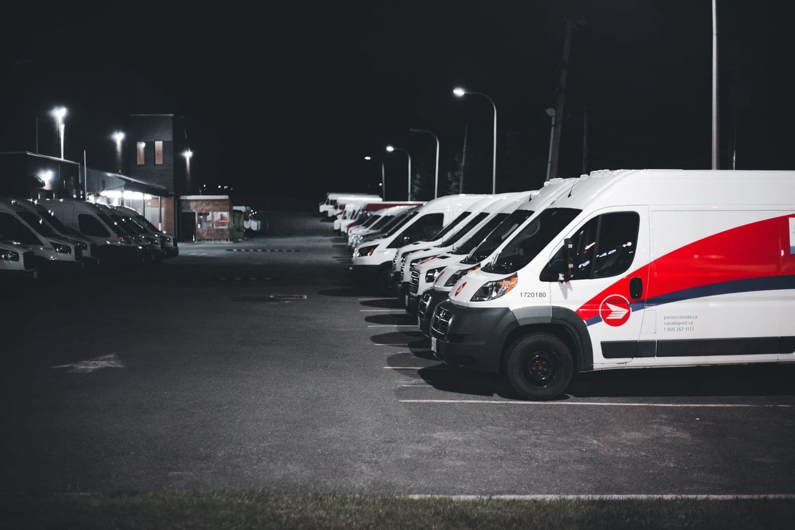 A line of transport vans parked at a depot before dawn