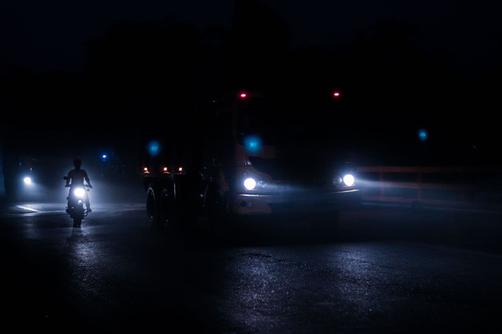 A truck running a dark highway at night, headlights cutting through haze